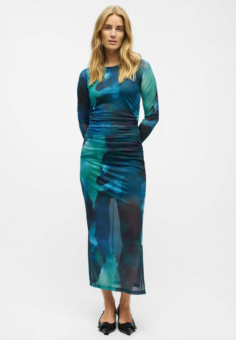 Robe à manches longues avec un imprimé abstrait bleu et vert, présentant un corsage ajusté, une taille froncée et une silhouette élégante et fluide.