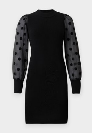 Juoda raukinėta suknelė su aukštu kaklu ir ilgomis permatomomis su taškeliais rankovėmis, prigludusios silueto, ir tvirtos juodos apykaklės rankovių galuose.