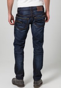 Mörkblå denimjeans med smal passform, kontrasterande sömmar, två bakfickor och en läderetikett i midjebandet.