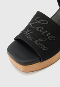 Μαύρο σανδάλι με πλατφόρμα και υφασμάτινη λωρίδα με κέντημα "Love Moschino", και ξ�ύλινη λεπτομέρεια στη βάση.