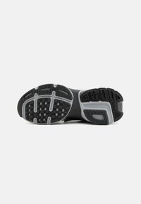 Suola di scarpa atletica nera con battistrada in gomma testurizzata, caratterizzata da scanalature e indentazioni a motivo, tallone rinforzato e distintivi accenti grigi.