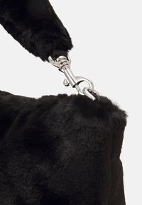 Zwarte handtas van nepbont met een zachte textuur, voorzien van een zilveren metalen gesp en een dikke handgreep voor veilig dragen.