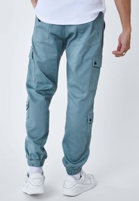 Pantaloni cargo azzurri con polsini elasticizzati, tasche laterali e tasche posteriori. Realizzati in tessuto morbido, presentano una vestibilità rilassata e cuciture su misura.
