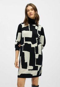 Schwarzes und cremefarbenes Strickkleid mit einem abstrakten geometrischen Muster, hohem Ausschnitt und langen Ärmeln mit gerippten Bündchen. Glatte Textur.
