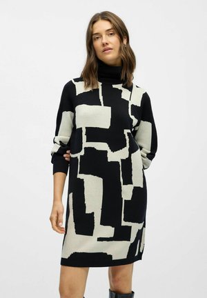 Robes en tricot noir et crème avec un motif géométrique abstrait, col montant et manches longues à bords côtelés. Texture douce.