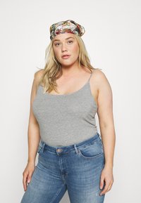 Grijze, aansluitende tanktop met dunne schouderbandjes, gedragen met hooggeknoopte blauwe spijkerbroeken. Haar gestyled met een kleurrijke, gemarmerde hoofddoek.