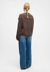 Rudas megztinis su apvaliu iškirpimu, derinamas su plačiomis mėlynomis džinsinėmis kelnėmis, turinčiomis tekstūruotą paviršių ir laisvą siluetą.