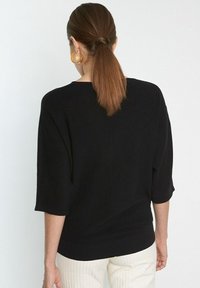 Czarny dzianinowy top o luźnym kroju, z rękawami o długości trzy czwarte i okrągłym dekoltem. Tekstura jest prążkowana, z gładkim wykończeniem z przodu.