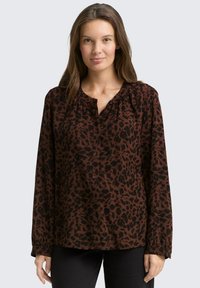 Blouse imprimé léopard marron et noir avec manches longues, encolure froncée et boutonnage sur le devant. Tissu doux avec une coupe décontractée.