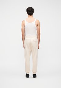 Άσπρο ανδρικό αμάνικο μπλουζάκι και μπεζ φόρμες, με χαλαρή εφαρμογή και λεπτομέρεια πίσω τσέπης. Μαύρα αθλητικά παπούτσια ολοκληρώνουν το σύνολο.