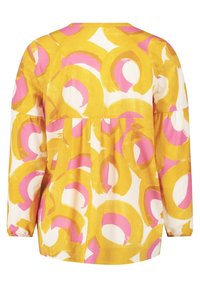 Haut à motifs jaunes et blancs avec des dessins circulaires roses et orange. Manches longues, coupe ample et détail froncé à la taille.