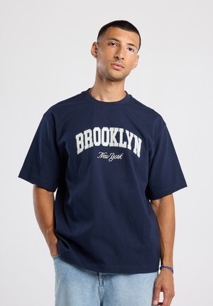 Navy blauwe katoenen t-shirt met "BROOKLYN New York" in contrasterende witte letters, korte mouwen en een ontspannen pasvorm.