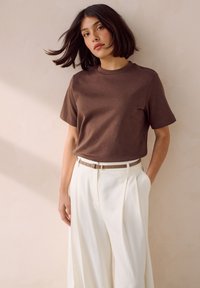 Camiseta marrón de manga corta combinada con pantalones blancos de cintura alta, con una textura suave y elegante y un cinturón de tono neutro.