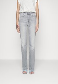 Světle šedé džíny rovného střihu s klasickým pětipocket designem, nošené s volně střiženým bílým topem a modrými sandály na otevřenou špičku.