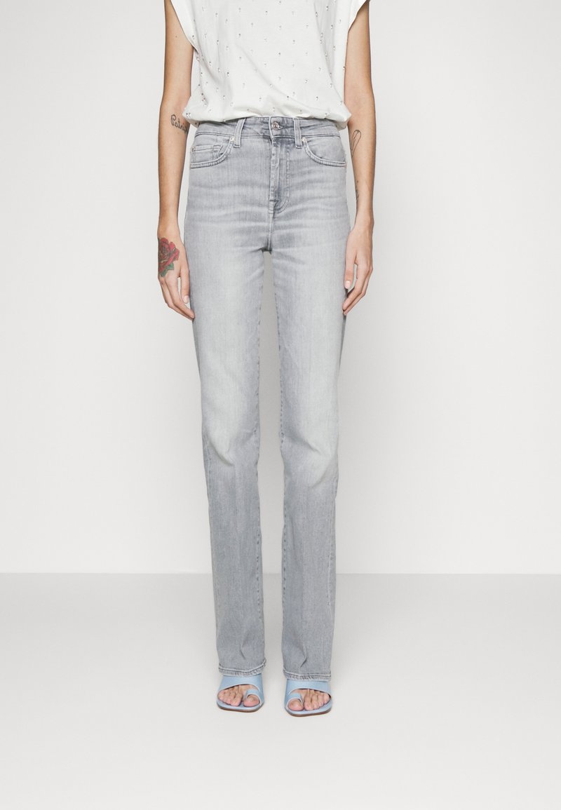 Světle šedé džíny rovného střihu s klasickým pětipocket designem, nošené s volně střiženým bílým topem a modrými sandály na otevřenou špičku.