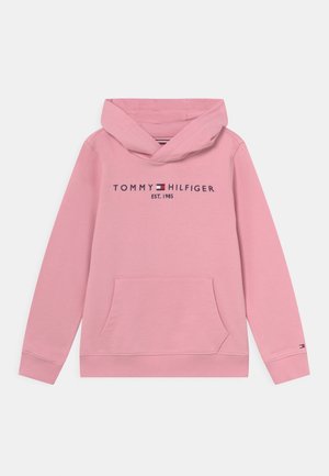 Różowa bluza z kapturem z kieszenią z przodu oraz logo "Tommy Hilfiger EST. 1985" w czerni, z detalem flagi w kolorach czerwonym, białym i niebieskim na piersi i mankiecie rękawa.