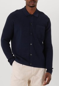 Navyblauwe geribbelde gebreide cardigan met een kraag, knoopsluiting en een borstzak. Beschikt over nauwsluitende lange mouwen en een gestructureerde vorm.