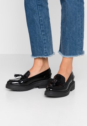 Sorte loafers i laklæder med en tyk sort plattformsål og dekorativ sløjfe foran. Klodset form, glat tekstur og blank finish.