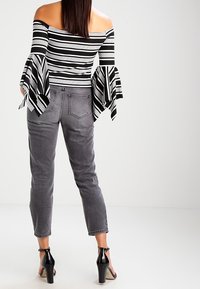 Top a righe bianco e nero senza spalle con maniche larghe, abbinato a jeans grigi a gamba stretta e sandali neri con tacco alto.