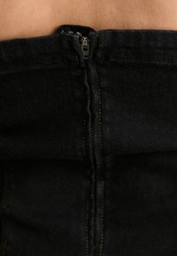 Μαύρο τζιν ύφασμα με κάθετη φερμουάρ κλείσιμο κατά μήκος της πλάτης. Διαθέτει λεία υφή και αντίθετες λεπτομέρειες σε αψεγάδιαστο ραφές.