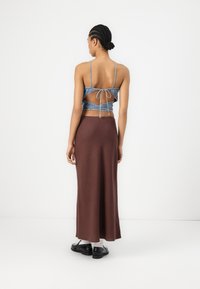 Denim crop top with open back, adjustable tie, and thin straps, paired with a long, fitted brown skirt, and black shoes. Smooth texture.