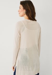 Maglione beige a maniche lunghe con orlo posteriore curvo, polsini a costine e pannello inferiore testurizzato, realizzato in morbido materiale a maglia leggera.