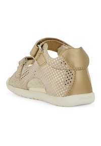 Sandalo in pelle perforata color tan con tallone chiuso, cinturino regolabile e suola bianca. Presenta piccoli fori circolari e dettagli in oro.