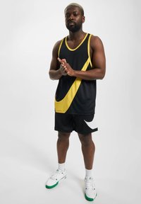 Svart treningssinglet med gul skråstripe, kombinert med sorte shorts med hvit swoosh. Brukt med hvite joggesko og grønne detaljer.