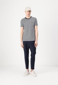 Csíkos t-shirt sötétkék és fehér színben, kerek nyakú, kis sárga logóval, amelyet sötétkék, keskenyített nadrággal és fehér tornacipővel párosítottak.