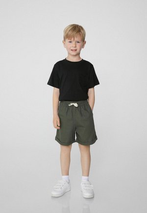 Černé tričko s krátkým rukávem a kapsou, olivové šortky se šňůrkou a bílé tenisky. Jednoduchý design, volný střih a ohrnutý lem šortek.