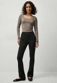 Lange mouwen, taupe top met een ronde hals, gecombineerd met zwarte, strakke broek. Beide kledingstukken zijn glad en rekbaar, wat het draagcomfort vergroot.