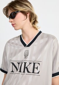 Light grey sports jersey with vertical stripes, black collar, and logo featuring "NIKE" prominently displayed. Soft texture, short sleeves.