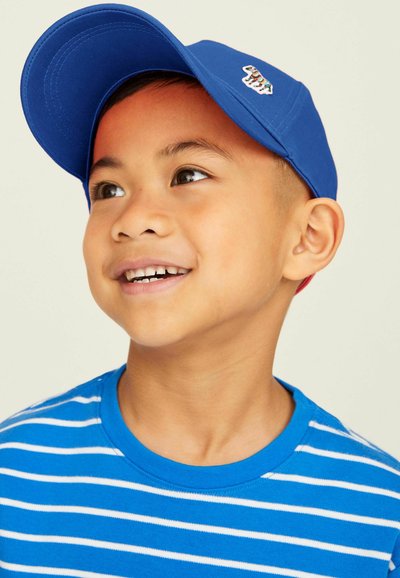 Kék baseball sapka egy kis folttal és kék-fehér csíkos póló. Az anyag puha és sima, kiemelve a laza dizájnt.