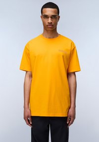Tričko s krátkým rukávem v jasně žluté barvě z bavlny, s malým logem na levé části hrudi. Rovný střih s kulatým výstřihem.