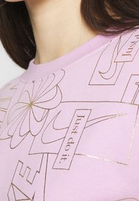 Lavendel sweatshirt med guldtryck som har blommotiv och frasen "Just do it." Rund halsringning och mjuk tygkvalitet.