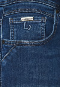 Granatowe dżinsy z tylną kieszenią z metalową etykietą "LANCERTO" oraz kontrastowym pomarańczowym przeszyciem wzdłuż szwów.