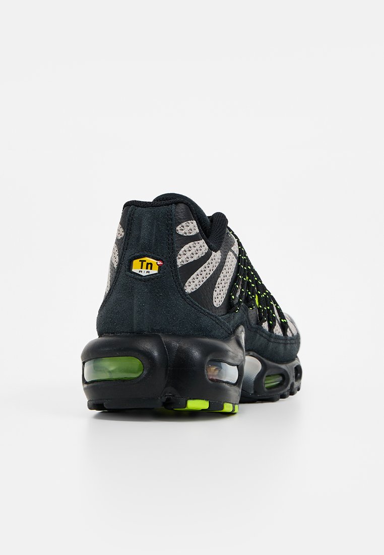 Scarpa sportiva nera con tomaia in rete, accenti riflettenti e imbottitura ad aria di un verde brillante. Presenta un distintivo logo Tn sul tallone.