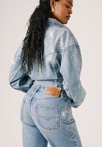 Leren spijkerjacket en spijkerbroek in lichtblauw met rhinestone patronen, hoge taille en een klassieke pasvorm. Bevat een merklabel op de achterzak.