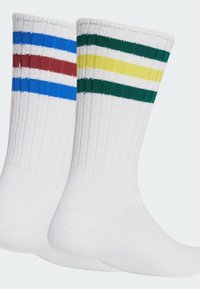 Białe skarpetki z żebrowaną strukturą i kolorowymi paskami: niebieskim i czerwonym na jednej skarpetce, zielonym i żółtym na drugiej.