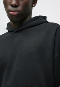 Μαύρη hoodie με άνετη εφαρμογή, κατασκευασμένη από μαλακό ύφασμα βαμβακερού μείγματος. Περιλαμβάνει μπροστινή τσέπη καγκουρό και κουκούλα με κορδόνια.