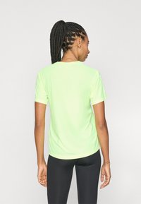 Korte mouwen, fel neon groene sportshirt met een ronde hals, een gladde textuur en een ontspannen pasvorm, gecombineerd met zwarte sportleggings.