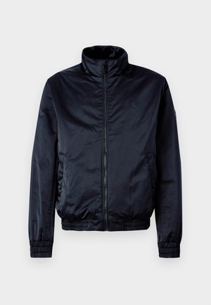 Námořnická modrá bomber bunda vyrobená z hladkého, lehkého materiálu, s předním zipem, vysokým límcem, pružnými manžetami a pasem.