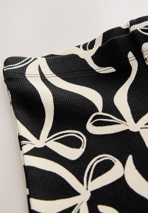 Sort stof med ribbet tekstur, der har et mønster af hvide sløjfer. Designet inkluderer smalle linjer og buede former for visuel interesse.