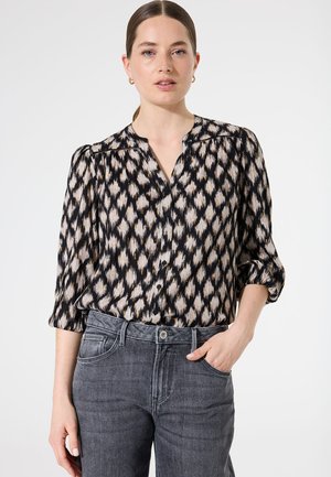 Blouse noire avec un motif géométrique crème, à manches longues, avec un devant à boutons et une coupe décontractée, assortie à un jean gris taille haute.
