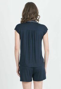 Top corto colore blu scuro con dettagli arricciati sul retro, abbinato a pantaloni corti coordinati. Tessuto morbido e liscio con una vestibilità comoda.