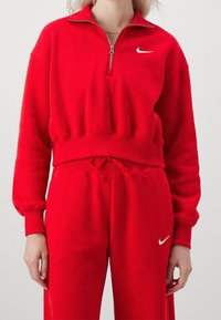 Röd zip-up sweatshirt med hög krage, ribbad mudd och midjeband, ihopparad med matchande mjukisbyxor med en vit Nike-logga.