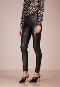 Black faux leather leggings with a sleek, fitted design and side zip detailing, paired with black mules featuring a pointed toe.