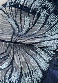 Marinfärgad nätväv med intrikat ljusblå blommönsterbroderi. Designen har en lagerstruktur och känsliga tråddetaljer.