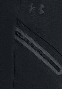 Black athletic joggers with a textured finish, featuring a side zip pocket and a subtle logo in the upper corner.