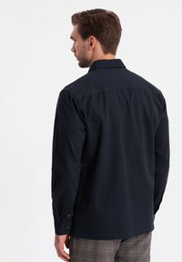 Camisa abotonada de un azul marino oscuro con cuello, mangas largas y puños abotonados. Textura suave y ajuste relajado, vista desde la parte posterior.